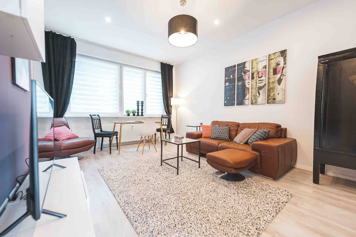 Offener Wohnbereich mit braunem Ledersofa, Glascouchtisch und Essplatz am Fenster