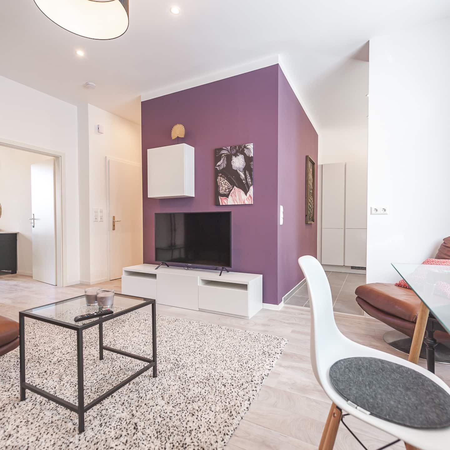 Wohnbereich mit auberginefarbener Akzentwand, Flat-TV und offenem Übergang zum Eingang