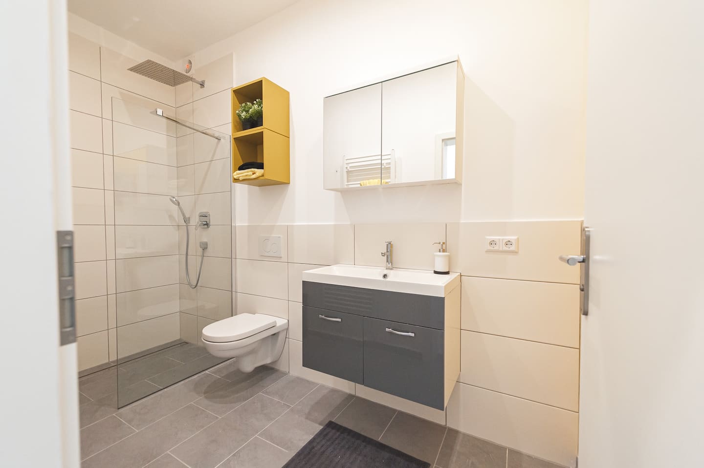 Modernes Bad mit ebenerdiger Regendusche, Wand-WC und Waschtisch mit Spiegelschrank